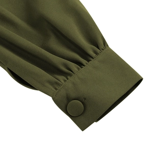 Détail de la manche d'une robe vert olive avec des plis et un bouton recouvert de tissu