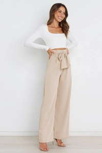 Detail view of high-waisted beige wide-leg trousers with a waist-tie bow and elegant drape