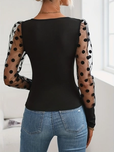 Macro detail of sheer mesh sleeve with elegant black flocked polka dots on slim top