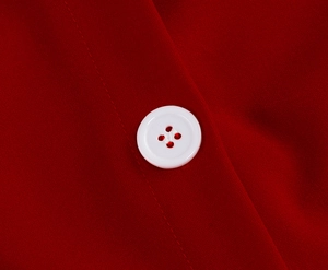 Detailed macro view of a white four-hole button on high-quality red textile fabric