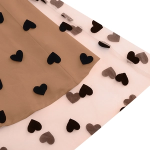 Detail view of white mesh overlay with black flocked heart patches on khaki dress fabric