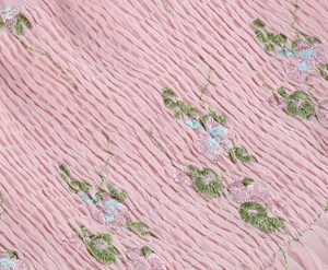 Detailed view of light pink mesh fabric with smocked texture and floral embroidery