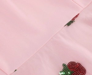 Detail of pink fabric featuring red and green sequin strawberry embroidery for cocktail dress