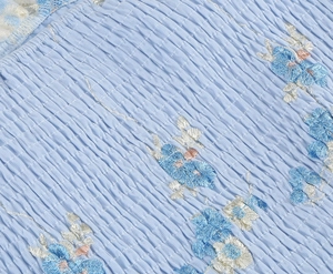 Detail of light blue smocked fabric featuring intricate floral embroidery on dress