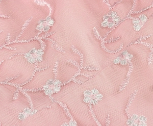 Gros plan sur un tissu en maille rose avec broderie florale blanche et motifs de vigne