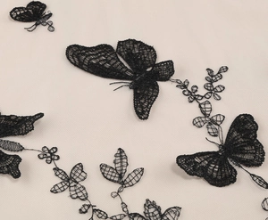 Detailed close-up of intricate black lace butterfly and floral embroidery on pink mesh fabric