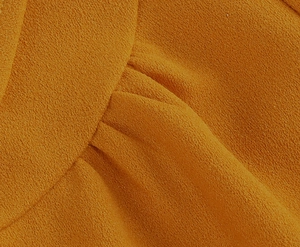 Detailed macro view of mustard yellow crepe fabric with elegant pleating texture