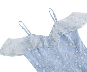 Détail de robe en tulle bleu clair avec broderies florales blanches et bretelles dentelle
