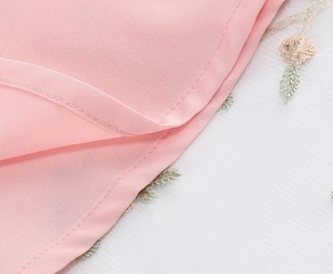 Detailed close-up of pink fabric with floral embroidery on white mesh overlay