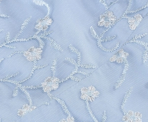 Détail du tissu en maille bleu clair avec broderie florale blanche pour robes élégantes