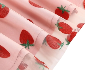 Detailed close-up of pink mesh dress fabric with red glitter strawberry embroidery