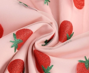 Detailed close-up of pink mesh fabric featuring shimmering glitter strawberry patterns