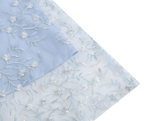 Vue macro du tissu en maille bleu clair avec broderie florale délicate et feuillage