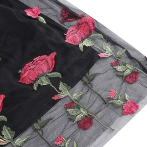 Detail of red rose floral embroidery on black mesh fabric with layered texture