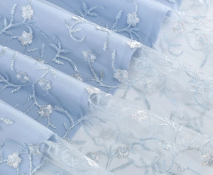 Gros plan sur un tissu en maille bleu clair avec broderie florale et texture de tulle multicouche