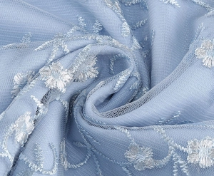 Détail du tissu en mesh bleu clair avec broderie florale blanche élégante et texture douce