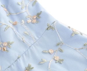 Close-up detail of light blue mesh fabric featuring delicate floral and leaf embroidery
