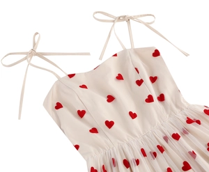 Close-up of white tie-shoulder strap dress with delicate red heart embroidery and tulle