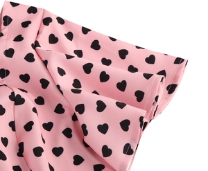 Detailed view of ruffle hem and black heart pattern on pink mid-length dress fabric