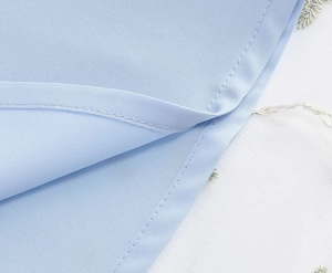Close-up of light blue fabric detail with precise double-needle stitching on the hem