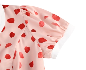 Close-up of pink dress showing puffy sleeve with red heart print and white Peter Pan collar