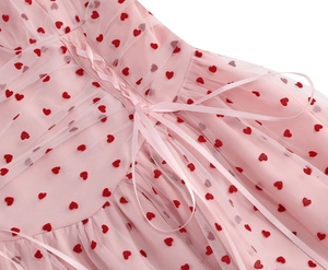 Dettaglio dell'abito in mesh rosa con ricami a cuore rossi e lacci in raso sulla schiena