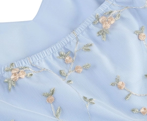 Close-up of pink floral embroidery on light blue mesh fabric with delicate tulle layers
