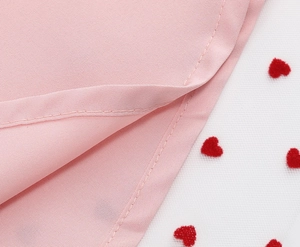 Dettaglio dell'orlo del vestito rosa con cuciture parallele e mesh a cuori rossi