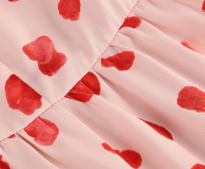 Detailed close-up of light pink dress fabric with red heart prints and shirred stitching details