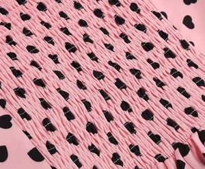 Detail view of pink smocking fabric with black heart prints on a vintage dress