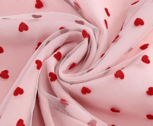 Dettaglio del tessuto a rete rosa con cuori rossi floccati e morbide pieghe naturali