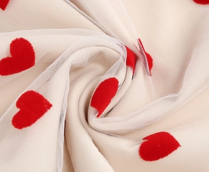 Detail of white mesh fabric with red flocked heart patterns for sweet summer dresses