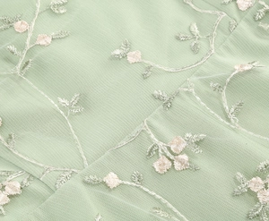 Detail of light green mesh fabric featuring exquisite 3D floral embroidery and silver threads