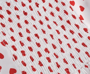 Detailed macro view of white fabric with red heart print and elastic smocked stitching