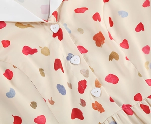 Detail view of heart-shaped white buttons and colorful prints on a beige summer dress