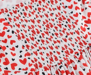 Détail du tissu smocké élastique avec imprimés cœurs rouges et noirs sur robe blanche