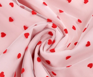 Detailed view of light pink tulle fabric with red flocked heart patterns for dress