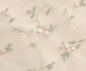 Close-up of champagne mesh fabric with intricate pink floral embroidery and green leaves