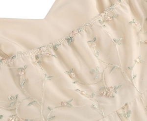 Detail of floral embroidery on beige tulle dress with elegant pleated V-neckline texture