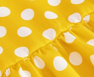Close-up of yellow polka dot fabric with ruffle details and fine stitching on kids dress