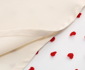Vista macro del tessuto beige con cuori rossi floccati su tulle a rete bianco