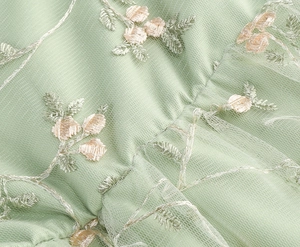 Détail du tissu en tulle vert clair avec une broderie florale délicate couleur champagne