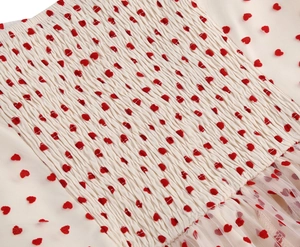 Dettaglio del tessuto mesh crema con cuori rossi e trama elastica a punto smock
