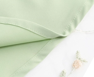Détail du tissu en satin vert clair avec coutures fines et broderie florale en tulle