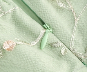 Détail de la maille vert clair avec broderie florale blanche et fermeture éclair invisible