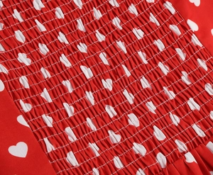 Close-up of red floral dress fabric featuring elastic smocking and white heart patterns
