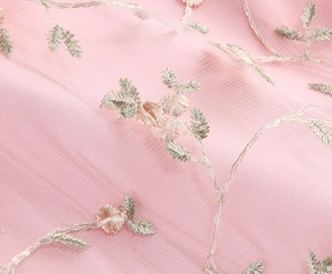 Détail de tulle rose pâle avec broderie florale délicate et fils de soie vert clair