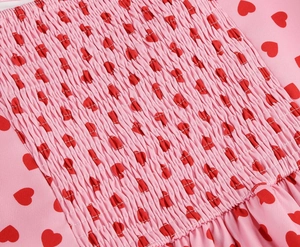 Detail of smocking process on pink fabric with red heart print and elastic pleats