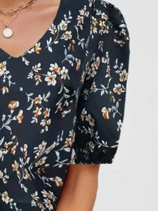 Close-up of V-neck floral top with puff sleeves and gold coin necklace detail