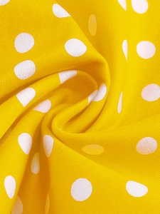 Gros plan d'un tissu jaune vif à pois blancs montrant la texture et les plis du textile